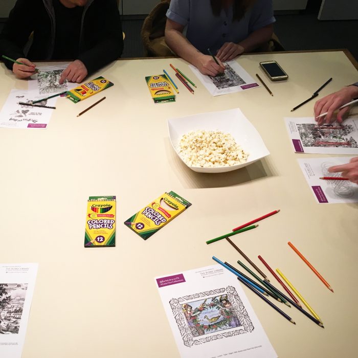 Photograph from the Color Our Collections 2019 coloring event at the Burke Library at Union Theological Seminary, Columbia University. Image shows a table with popcorn and people's hands holding pencils and coloring in images on paper