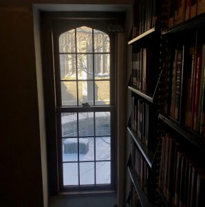 Photograph by Hannah Ervin, of a window seen from inside the Burke Library book shelving area, looking out onto the Union Theological Seminary quadrangle ("the quad") with visible construction scaffolding along the exterior walls