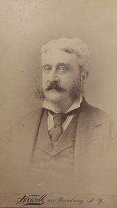 White-haired man with a dark mustache and sideburns in a three-piece suit.